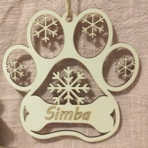 Décoration de Noël en bois clair en forme de patte de chien, gravée du prénom de votre animal (comme "Simba" sur le modèle). Le design hivernal est sublimé par de délicats flocons de neige découpés au laser et une zone en forme d'os pour le texte. C'est le souvenir parfait ou le cadeau idéal pour tout amoureux des chiens.